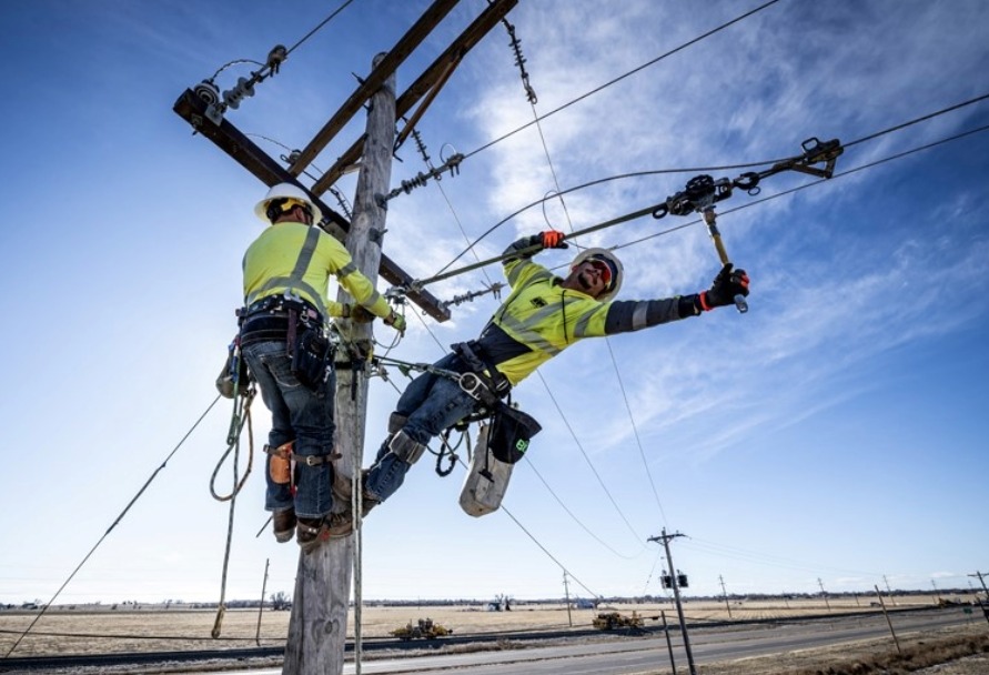 Two linemen working at the top of a power pole